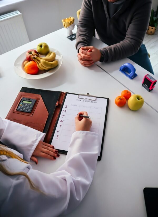 A nutritionist writes a weekly meal plan for a client in an office setting, surrounded by fresh fruits.