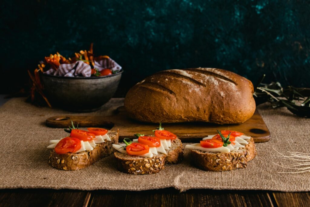 A rustic loaf accompanied by multigrain bread slices topped with cheese and tomatoes in a cozy setting.